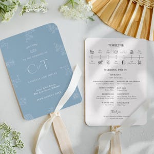 Puede incluir: Dos programas de abanico de boda. Uno es azul claro con detalles florales y el texto "WELCOME TO THE WEDDING OF CT CAMILLE AND TOBIAS". El otro es blanco con una línea de tiempo y detalles de la fiesta de bodas. Ambos tienen cinta color crema.