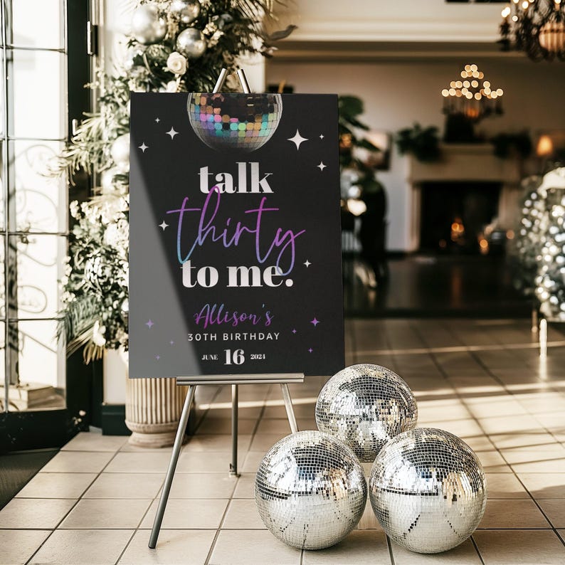 May include: A black sign on an easel with the text "talk thirty to me." The sign also includes the name "Allison's" and the date "June 16, 2021." Three disco balls are on the floor in front of the sign.