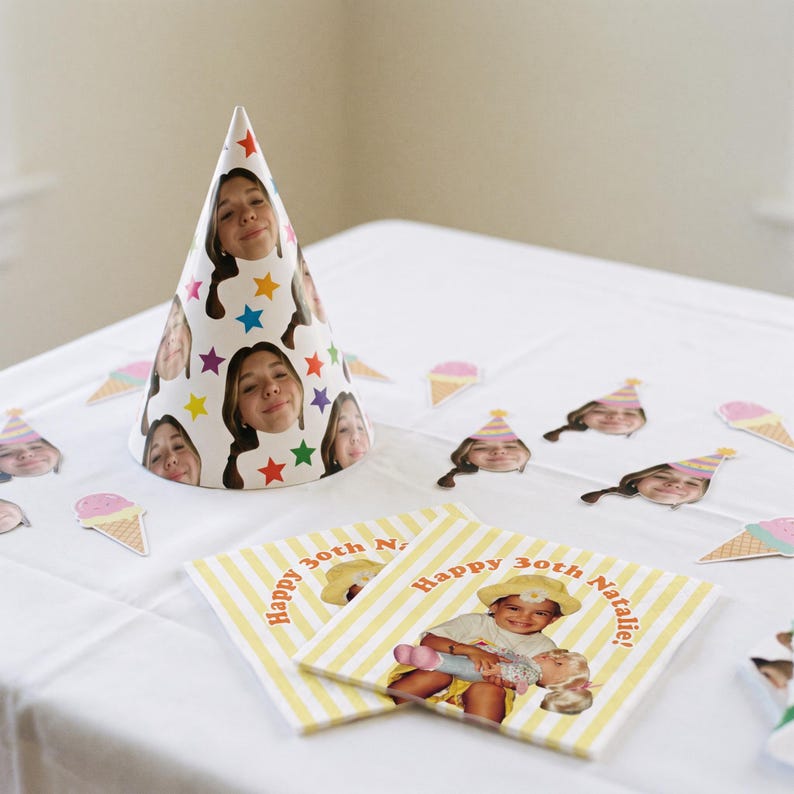 May include: A conical party hat featuring a repeating pattern of a person's face and colorful stars, accompanied by square paper napkins with yellow and white stripes, the text Happy 30th Natalie!, and a photo of a child holding a doll.