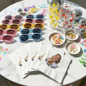 May include: A collection of party supplies including sunglasses, decorative glasses, small decorative plates, and napkins. The sunglasses are in pink, yellow, and blue. The glasses have lemon, cherry, and watermelon designs. The napkins have the text "DO YOUR THING 21".