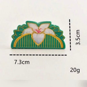 May include: A green and gold hair comb with a white flower design. The comb is 7.3 cm wide and 3.5 cm tall and weighs 20 grams.