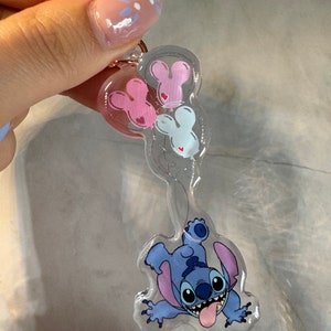 K&ouml;nnte beinhalten: Ein transparenter blauer Stitch-Schl&uuml;sselanh&auml;nger mit einem rosa, wei&szlig;en und blauen Mickey-Maus-Ballon-Anh&auml;nger. Der Schl&uuml;sselanh&auml;nger hat einen ros&eacute;goldenen herzf&ouml;rmigen Ring.