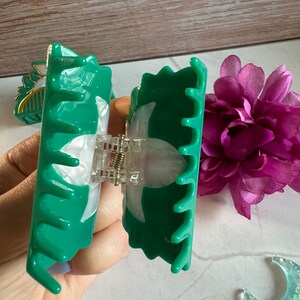 May include: A green plastic hair claw with a white swirl design. The claw is open and ready to be used to hold hair in place.