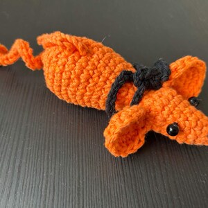 May include: A crocheted orange mouse toy with black eyes and a black crocheted band around its head.