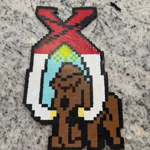 May include: A brown pixel art figure with a red, white, and blue pixel art hat. The figure is holding a white pixel art object in each hand. The figure is standing on a gray background.
