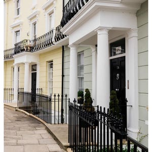 May include: Row of townhouses with black wrought iron railings and balconies. The buildings are painted in pastel yellow and green with white columns and trim. The front doors are black, and the address number 24 is visible.