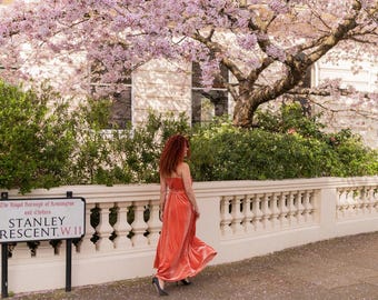 Una mujer con un vaporoso vestido color coral caminando bajo un cerezo en flor en Notting Hill, Londres. Impresión artística giclée.