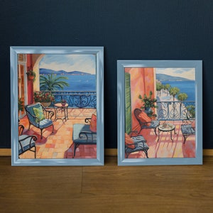 Puede incluir: Dos pinturas enmarcadas que representan escenas al aire libre con balcones y muebles. Las pinturas están en marcos azules y presentan una combinación de colores azul y blanco.
