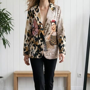 Op de afbeelding: Een blazer met lange mouwen en een mixed-media ontwerp met een opvallende luipaardprint aan de linkerkant en een beige paneel aan de rechterkant. De rechterkant toont een portret van Frida Kahlo, bloemaccenten en vintage tekstafbeeldingen.