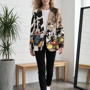 Könnte beinhalten: Ein Blazer mit geteiltem Design, bestehend aus einem braun-weißen Zebramuster auf der linken Seite und einem beigen Paneel mit mehreren Mickey-Maus-Grafiken auf der rechten Seite, getragen über einem schlichten weißen T-Shirt und einer schwarzen Hose.