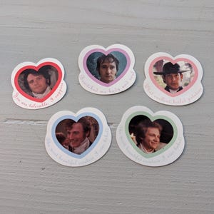 May include: Five heart-shaped stickers featuring portraits of actors. Each sticker has a different colored border and a quote from a movie. The stickers are white with a light gray background.