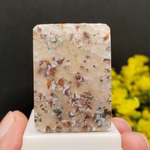 May include: A rectangular polished stone cabochon with a translucent, milky off-white base. The surface features scattered, irregular inclusions in shades of deep red, rust orange, dark brown, and small flecks of pale green throughout the stone.