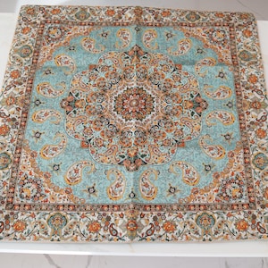 May include: A square textile featuring a central medallion and intricate paisley patterns in shades of light blue, orange, black, and cream. The design includes a detailed border with repeating floral motifs and teardrop shapes throughout the fabric.