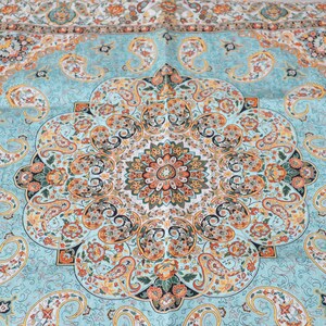 May include: A textile featuring a central circular medallion surrounded by intricate paisley motifs and floral patterns. The color palette consists of light blue, orange, yellow, and black, with a repeating border design along the top edge.