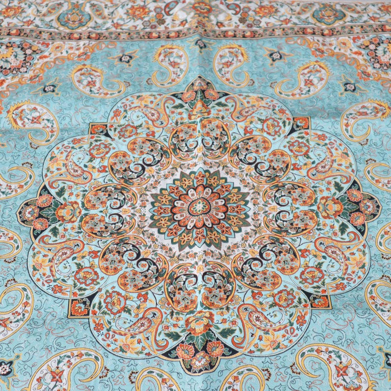 May include: A textile featuring a central circular medallion surrounded by intricate paisley motifs and floral patterns. The color palette consists of light blue, orange, yellow, and black, with a repeating border design along the top edge.