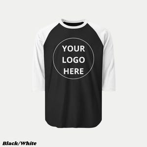 Pu&ograve; includere: Maglietta da baseball raglan bianca e nera con maniche a tre quarti. La maglietta ha un corpo nero, maniche e scollo bianchi. Un cerchio bianco sul davanti mostra il testo "YOUR LOGO HERE". Le parole "Black/White" sono in basso.