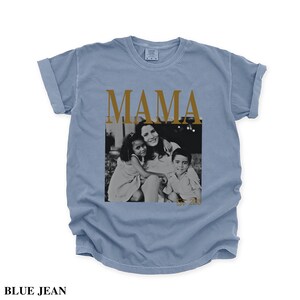 Puede incluir: Una camiseta azul vaquero con la palabra "MAMA" en letras doradas. La camiseta presenta una foto en blanco y negro de una madre y dos hijos. El texto "BLUE JEAN" est&aacute; en la parte inferior de la camiseta.