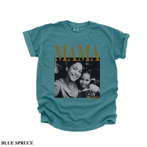 Puede incluir: Camiseta azul abeto con la palabra "MAMA" en letras doradas. Una foto en blanco y negro de una madre y un ni&ntilde;o sonriendo est&aacute; centrada debajo. La camiseta tiene las mangas enrolladas.