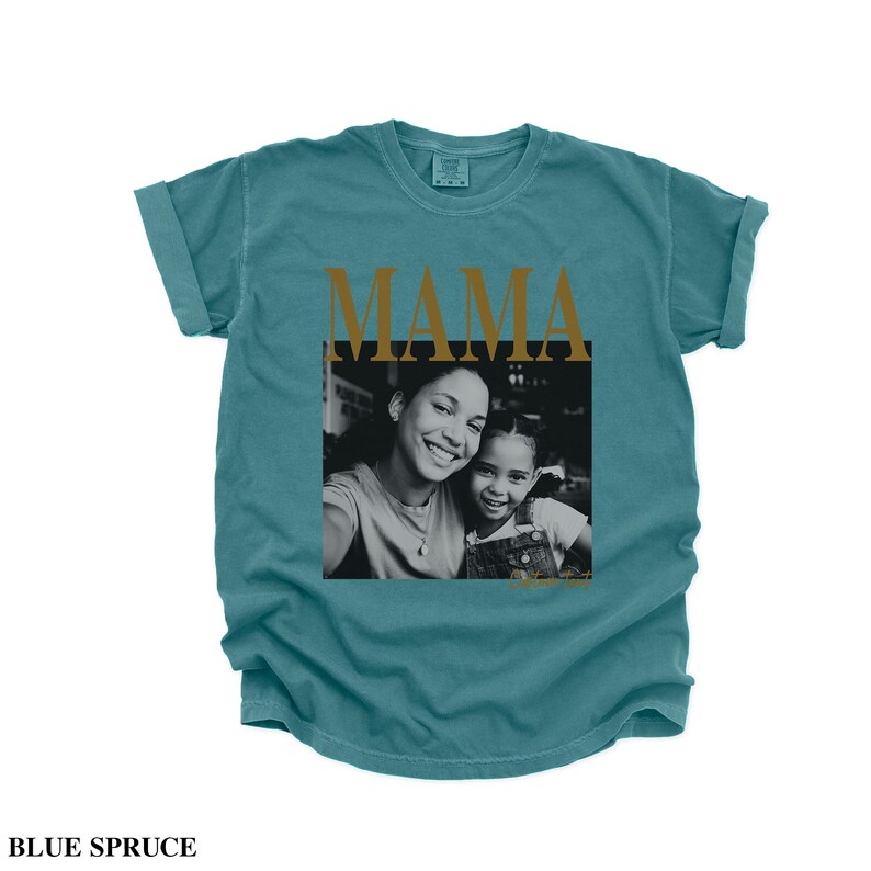 Puede incluir: Camiseta azul abeto con la palabra "MAMA" en letras doradas. Una foto en blanco y negro de una madre y un ni&ntilde;o sonriendo est&aacute; centrada debajo. La camiseta tiene las mangas enrolladas.