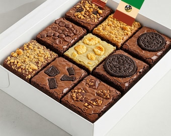 Może przedstawiać: Białe pudełko wypełnione dziewięcioma różnymi rodzajami brownie. Brownie są ułożone w siatkę 3x3. Każdy brownie ma inny dodatek, w tym wiórki czekoladowe, orzechy i Oreo.