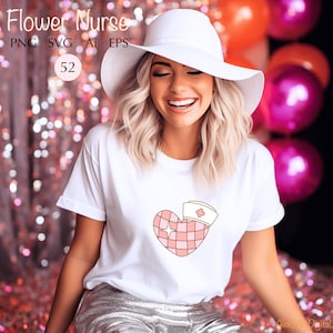 May include: A woman wearing a white t-shirt with a pink heart design featuring a nurse's hat. The heart is checkered and has a small star in the center. The text "Flower Nurse" is visible at the top of the image.