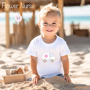 May include: A young child wearing a white t-shirt with a cartoon ambulance graphic. The ambulance is white with a pink cross and yellow wheels. The child is sitting on a sandy beach.