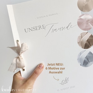 Könnte beinhalten: Ein weißes Hochzeitsalbum mit den Worten "UNSERE Traurede" in grauer Schrift. Das Album ist mit einem cremefarbenen Band gebunden. Der Text "SVENJA & MARKUS" steht über dem Titel. Das Album trägt den Text "Jetzt NEU: 6 Motive zur Auswahl" und das Datum "10. AUGUST 2025".