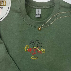 May include: A green sweatshirt with a black, red, and yellow embroidered Mickey Mouse design. The sweatshirt has a crew neck and long sleeves.