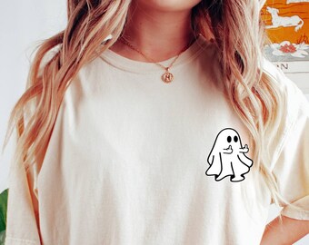 May include: A cream colored t-shirt with a black and white cartoon ghost giving a thumbs up. The ghost is on the left side of the shirt.