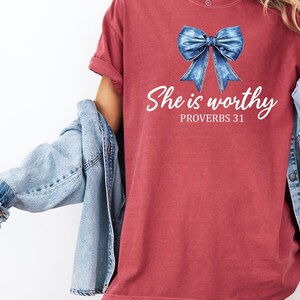May include: A red t-shirt with a blue denim bow and the text "She is worthy Proverbs 31" printed on the front.