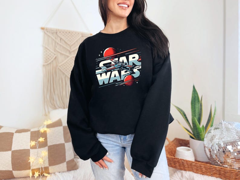 Puede incluir: Sudadera negra recortada con un gr&aacute;fico de una nave espacial volando por el espacio con el texto "Star Wars" en una fuente retro.