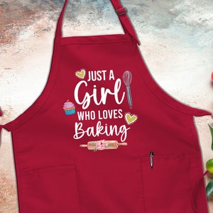 May include: Red apron with a white graphic that says "Just a Girl Who Loves Baking". The graphic includes a cupcake, a whisk, and a rolling pin.