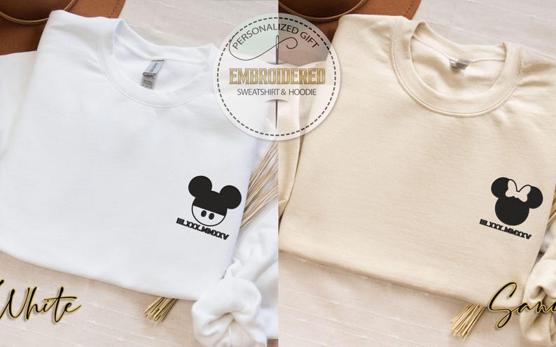 May include: White and beige sweatshirts with embroidered cartoon character designs. The white sweatshirt features a Mickey Mouse design, while the beige one has a Minnie Mouse design. Both have the text "BLXXX.MMXXV" below the designs.