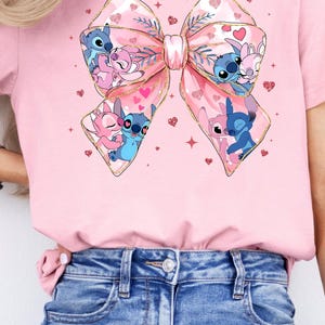 Peut inclure: T-shirt rose avec un grand n&oelig;ud rose avec des paillettes dor&eacute;es et un couple de personnages Stitch &agrave; l'int&eacute;rieur. Les personnages Stitch sont bleus et roses et s'embrassent. L'arri&egrave;re-plan est rose avec de petits c&oelig;urs roses et des paillettes dor&eacute;es.