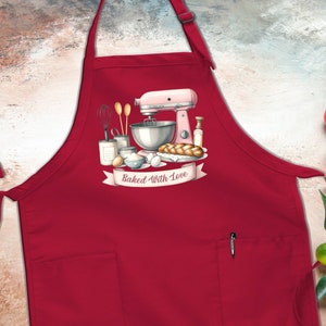 May include: Red kitchen apron with a pocket and a graphic of a pink stand mixer, ingredients, and a loaf of bread with the text "Baked With Love".