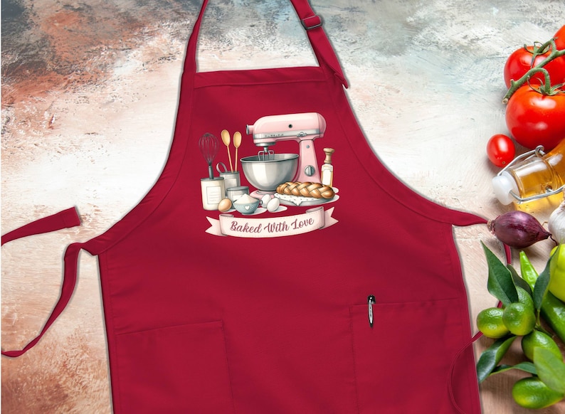 May include: Red kitchen apron with a pocket and a graphic of a pink stand mixer, ingredients, and a loaf of bread with the text "Baked With Love".
