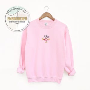 May include: Pink sweatshirt with a small embroidered image of Mickey Mouse in the center of the chest.