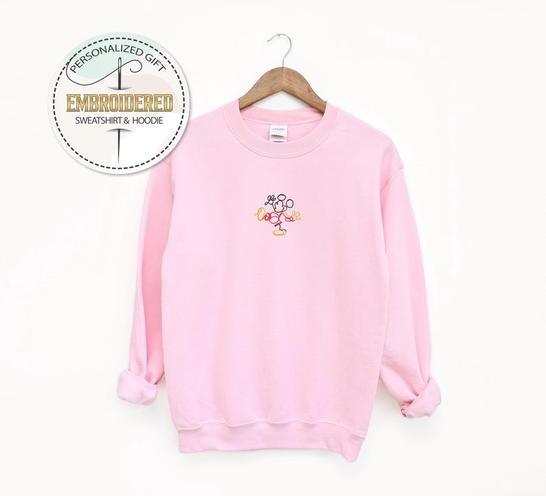 May include: Pink sweatshirt with a small embroidered image of Mickey Mouse in the center of the chest.