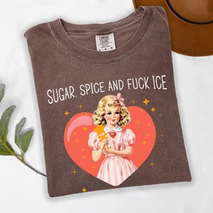 May include: Brown t-shirt with the text "SUGAR. SPICE AND FUCK ICE" in white. The shirt features a vintage illustration of a girl in a pink dress holding a star wand inside a red heart with gold stars.