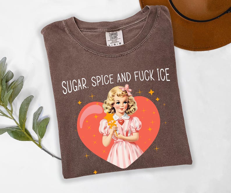 May include: Brown t-shirt with the text "SUGAR. SPICE AND FUCK ICE" in white. The shirt features a vintage illustration of a girl in a pink dress holding a star wand inside a red heart with gold stars.