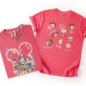 May include: Two red t-shirts featuring Disney's Toy Story characters. One shirt has a Mickey Mouse head design with characters like Woody, Buzz Lightyear, and others. The second shirt displays various Toy Story characters with their names.