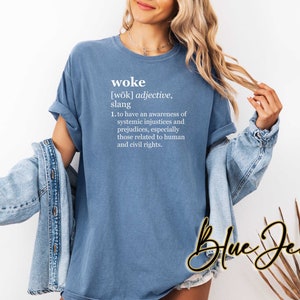 May include: A blue t-shirt with the definition of the word "woke" printed on it. The definition reads: "[wōk] adjective, slang 1. to have an awareness of systemic injustices and prejudices, especially those related to human and civil rights."