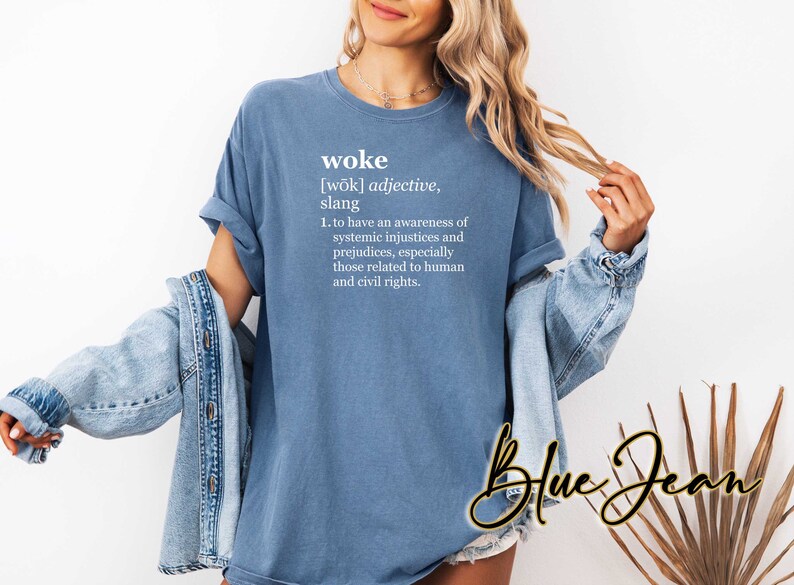 May include: A blue t-shirt with the definition of the word "woke" printed on it. The definition reads: "[wōk] adjective, slang 1. to have an awareness of systemic injustices and prejudices, especially those related to human and civil rights."