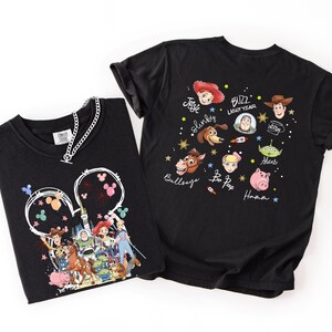 May include: Two black t-shirts with Toy Story designs. One shows characters within a Mickey Mouse outline with fireworks. The other has character faces and names such as Buzz Lightyear and Woody. A silver chain necklace is on the first shirt.