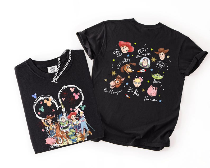 May include: Two black t-shirts with Toy Story designs. One shows characters within a Mickey Mouse outline with fireworks. The other has character faces and names such as Buzz Lightyear and Woody. A silver chain necklace is on the first shirt.
