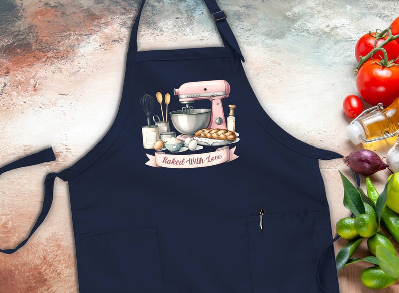 May include: A navy blue apron with a large pocket and adjustable straps. The apron features a pink stand mixer, bread, and other baking supplies with the text "Baked With Love".