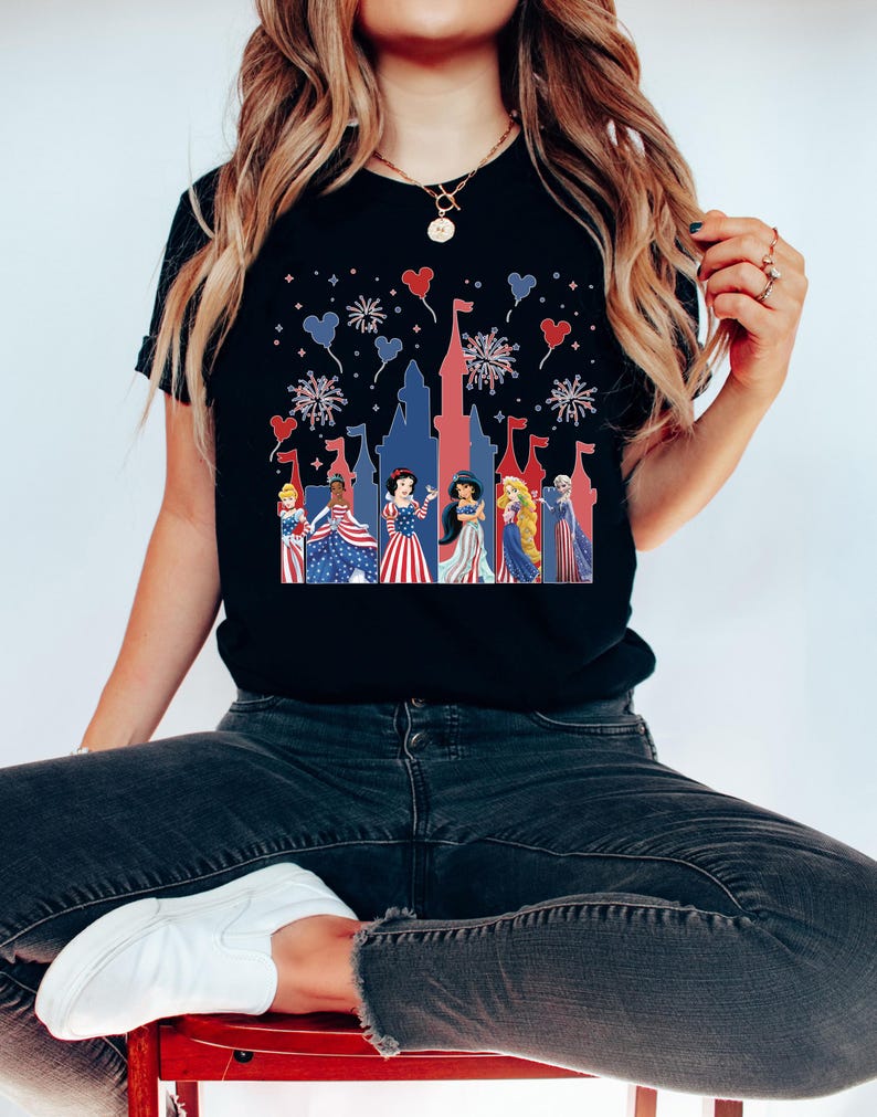 May include: Black t-shirt featuring a patriotic design with a castle silhouette and fireworks. The graphic includes several princesses in red, white, and blue attire. The design is festive and suitable for Independence Day celebrations.