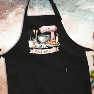 May include: Black apron with a pocket and a white graphic of a pink stand mixer, ingredients, and bread with the text "Baked With Love".