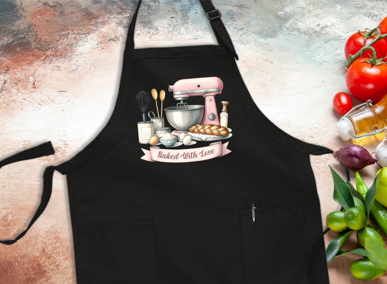May include: Black apron with a pocket and a white graphic of a pink stand mixer, ingredients, and bread with the text "Baked With Love".