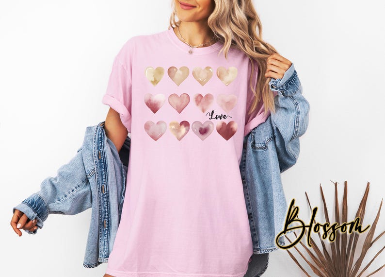 Puede incluir: Una camiseta rosa con un dise&ntilde;o de acuarela de corazones en tonos rosa y dorado. Los corazones est&aacute;n dispuestos en una cuadr&iacute;cula y la palabra "Love" est&aacute; escrita en letra negra debajo de los corazones.